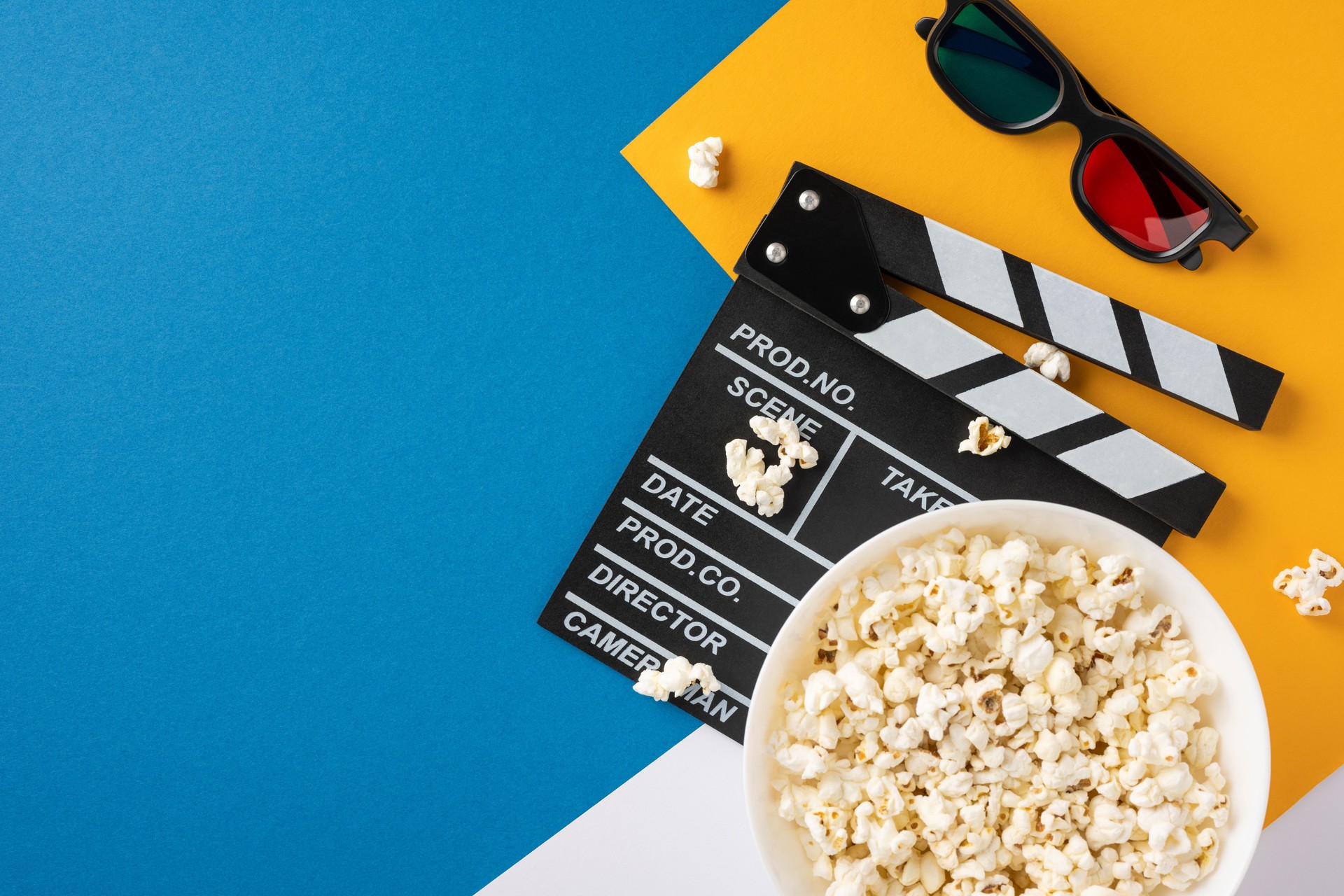A high-angle view of popcorn, a clapperboard, and 3D glasses on a colorful background, symbolizing the excitement of watching films